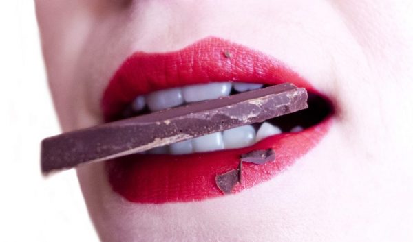 Zahnschmerzen durch Süßigkeiten? Frau mit Schokolade zwischen den Zähnen